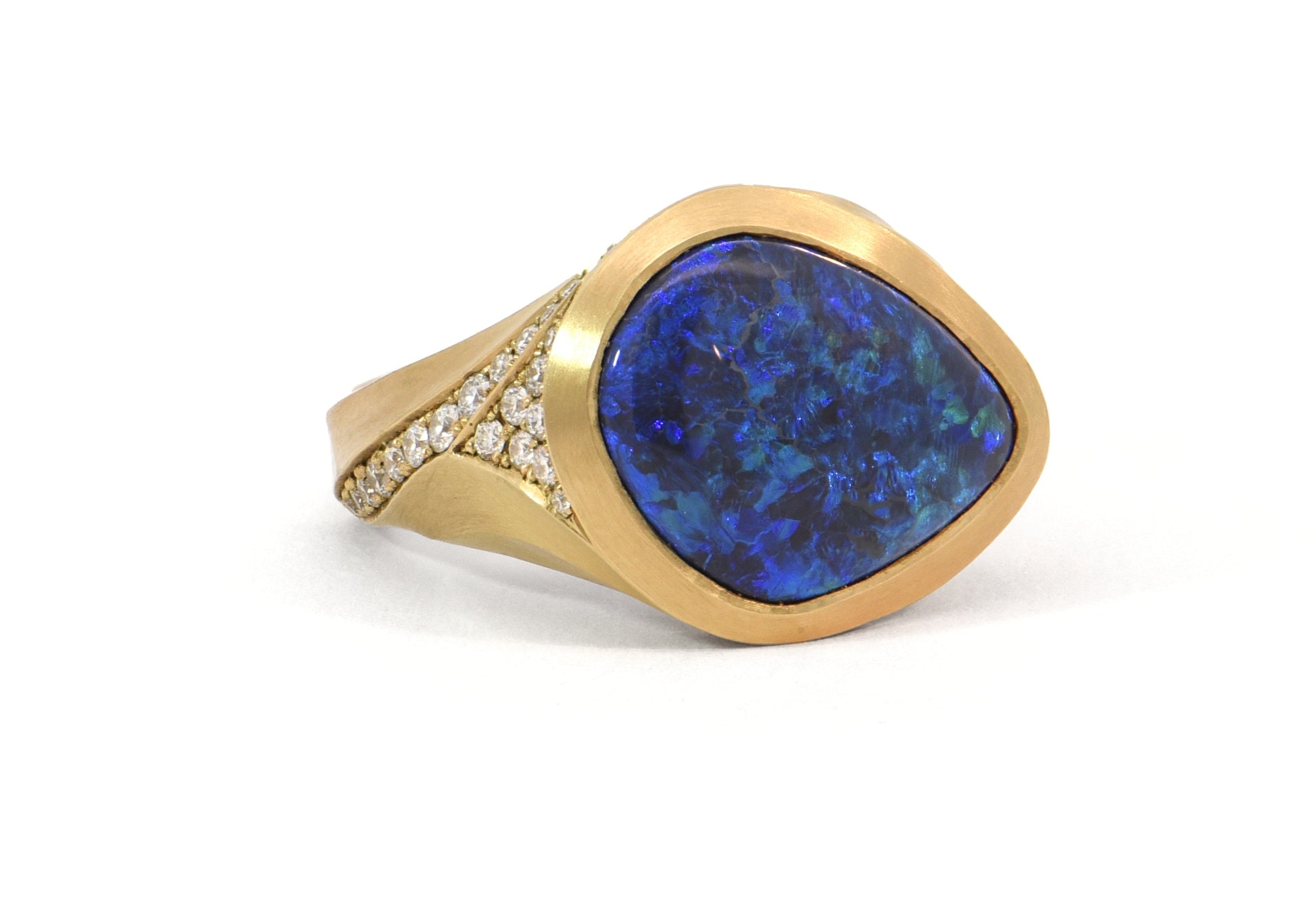 An 18 carat yellow gold Arris cocktail ring set with a black opal from Lightning Ridge, Australia, surrounded by a wide yellow gold bezel and enhanced by pave-set sparkling white diamonds along the sides.