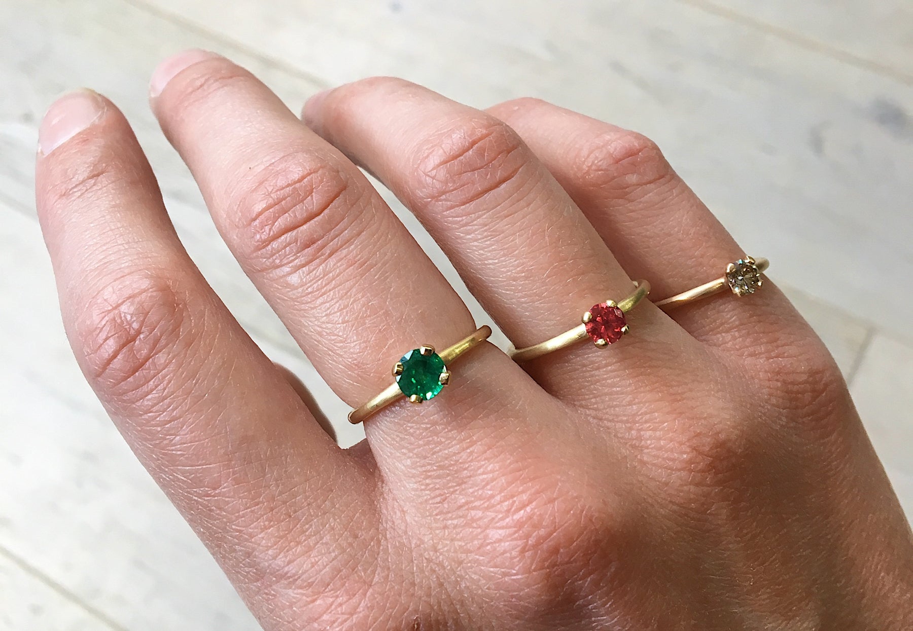 4 claw emerald, ruby and cognac diamond and yellow gold engagement rings on hand 